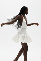 Mini robe crochet halter blanc en mouvement gracieux - vue de profil latéral montrant la fluidité du crochet ajouré, la silhouette mini qui met en valeur les jambes, et l'élégance bohème de la coupe halter - Style éditorial estival accessible - Vêtements élégants à prix doux Black-Coat