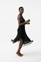 Robe cover-up crochet noir en mouvement gracieux - vue de profil latéral montrant la fluidité du coton ajouré noir, la fente latérale sensuelle qui révèle la jambe, les détails franges bohèmes en bas de robe, et la silhouette élégante sans manches - Style éditorial bohème chic accessible - Vêtements élégants à prix doux Black-Coat