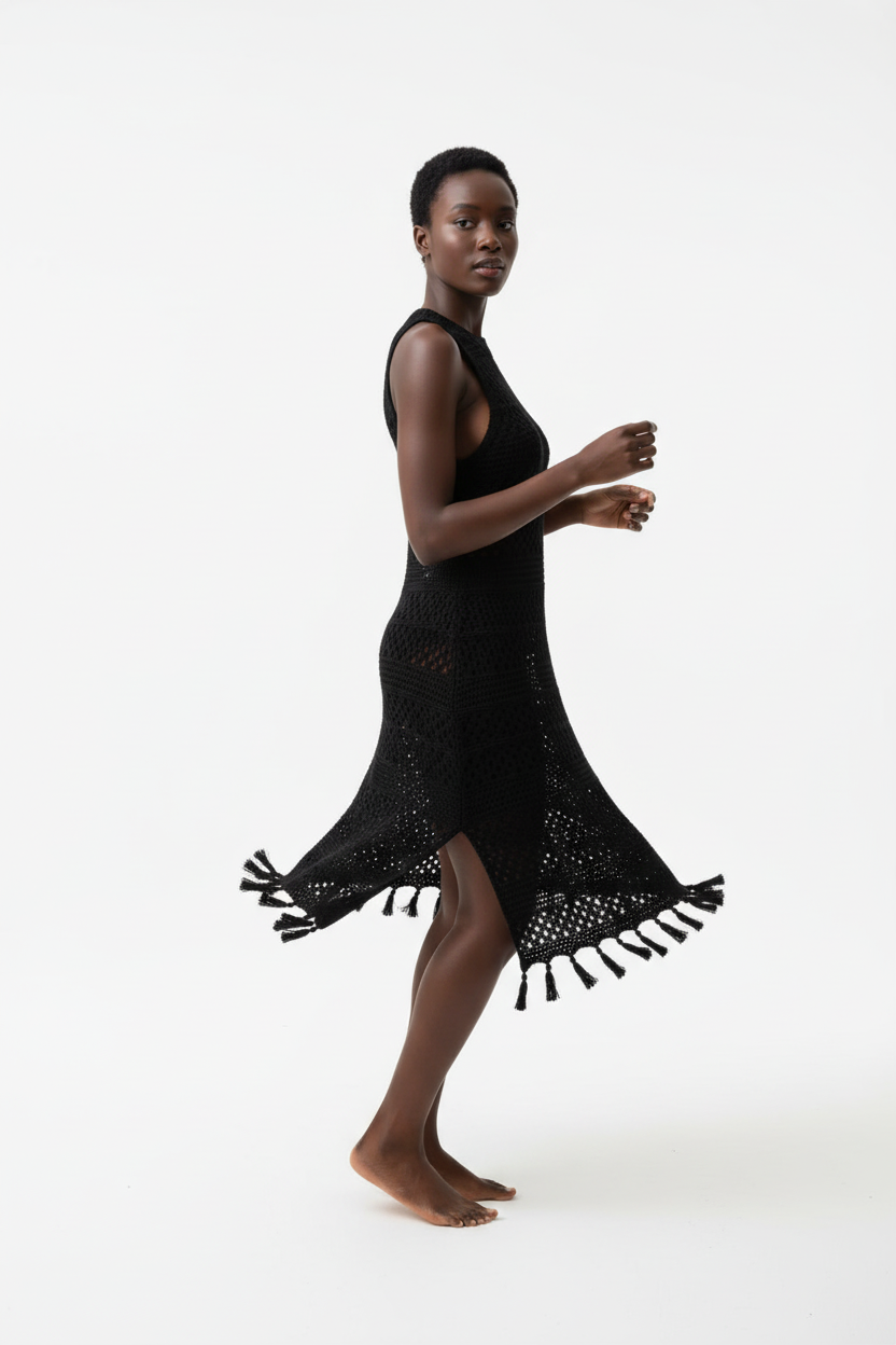 Robe cover-up crochet noir en mouvement gracieux - vue de profil latéral montrant la fluidité du coton ajouré noir, la fente latérale sensuelle qui révèle la jambe, les détails franges bohèmes en bas de robe, et la silhouette élégante sans manches - Style éditorial bohème chic accessible - Vêtements élégants à prix doux Black-Coat