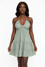 Robe mini halter smockée vert sauge avec col V profond à fronces empire, dos smocké ajustable avec laçage halter et trois niveaux de volants étagés - vue de face complète sur fond blanc studio montrant la silhouette romantique et féminine, le tissu 100% polyester léger en vert sauge apaisant et naturel - Mannequin en pose estivale élégante - Collection mode féminine accessible premium Black-Coat