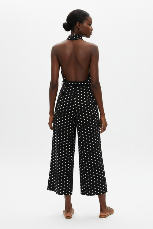 Vue arrière de la combinaison halter à pois noire sur fond blanc studio - dos révélant le dos ouvert élégant du halter, le laçage dans la nuque, et les jambes larges palazzo fluides en noir à pois blancs - Détail du design chic et estival - Style premium Black-Coat
