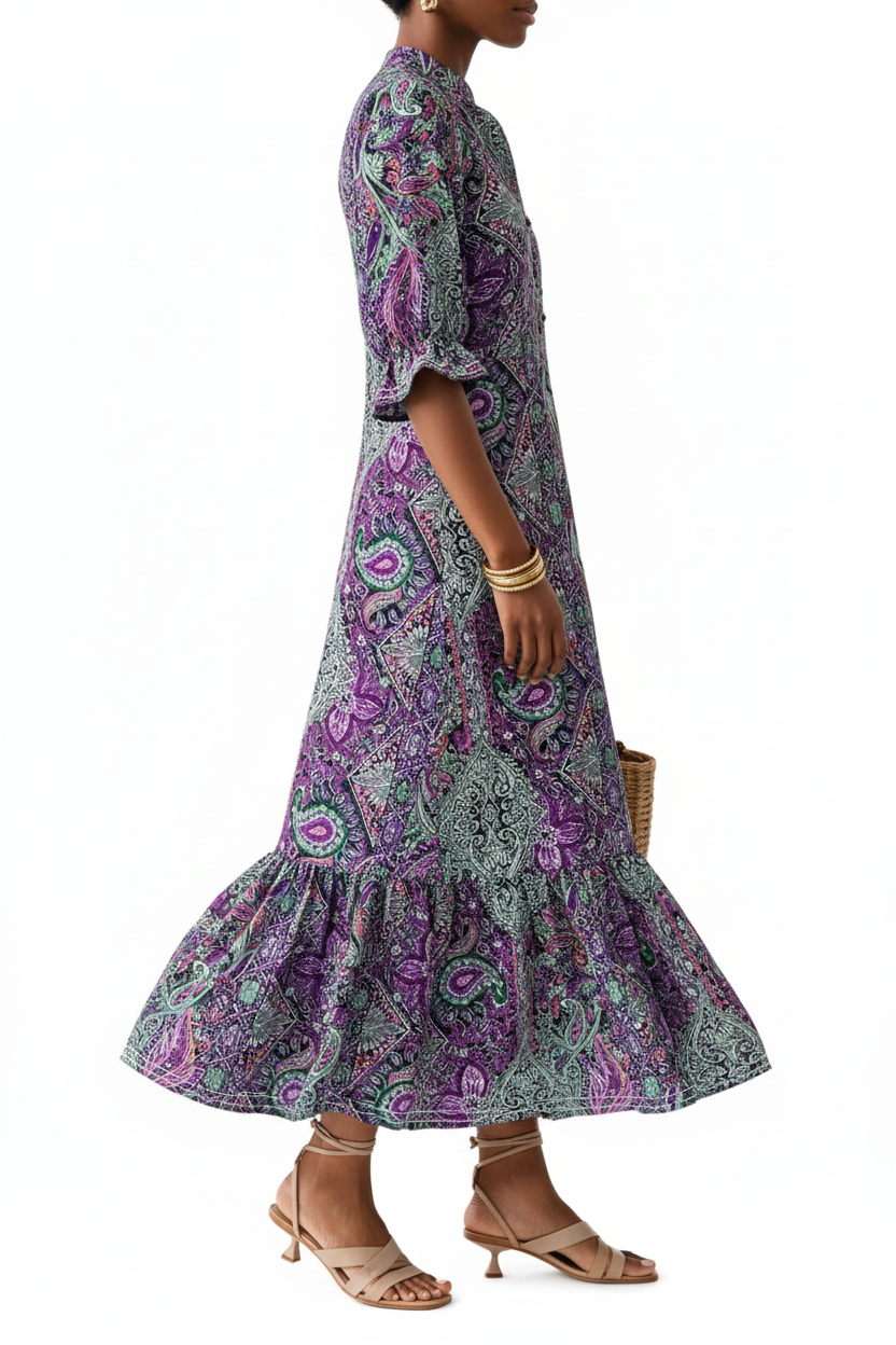 Vue de profil plein pied en mouvement robe midi bohème imprimé paisley violet prune à col V boutonné, manches 3/4 bouffantes et jupe étagée volantée — silhouette élégante révélant la richesse de l'imprimé paisley exclusif, le profil des manches bouffantes et la jupe étagée virevolant avec grâce — bracelets dorés, sac panier tressé, sandales plates beige — Silhouette-Chic