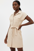 Vue trois-quarts de la robe chemise mini boutonnée col chemisier en abricot beige sur fond blanc studio - angle mettant en valeur le col chemisier pointu sophistiqué, la poche poitrine patch utilitaire et la ceinture nouée sculpturale en abricot beige chaud - Détail de la construction haut de gamme - Style éditorial Black-Coat