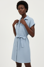 Vue trois-quarts de la robe chemise mini boutonnée col chemisier en bleu ciel sur fond blanc studio - angle mettant en valeur le col chemisier pointu sophistiqué et la poche poitrine patch utilitaire chic - Détail de la construction haut de gamme - Style éditorial Black-Coat