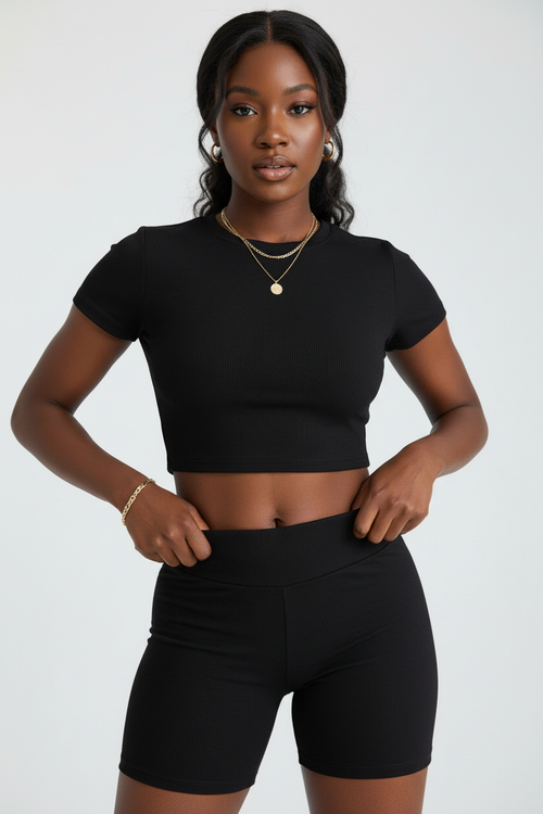 Gros plan détaillé de l'ensemble deux pièces noir - vue rapprochée montrant le détail du crop top col rond avec les fronces latérales qui sculptent la taille, la ceinture taille haute du short assorti, et les finitions premium du tissu polyester extensible - Détail de la construction haut de gamme - Style premium Silhouette-Chic