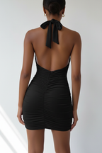Vue arrière spectaculaire de la robe mini bodycon halter noir sur fond blanc studio - dos nu intégral révélant le laçage halter élégant dans la nuque, la peau mise en valeur avec audace, et les fronces all-over qui continuent dans le dos - Détail du design sensuel et inoubliable - Style premium Black-Coat