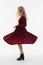 "Robe mini velours bordeaux col volant - en mouvement twirl montrant la jupe mini évasée qui tourne et s'ouvre, tissu velours fluide en mouvement dynamique, col à volants, texture bordeaux riche, fond blanc studio Silhouette-chic