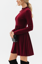 "Robe mini velours bordeaux col volant - vue de profil latéral montrant la silhouette ajustée évasée, col à volants visible de côté, jupe mini ligne A fluide, texture velours riche bordeaux, fond blanc studio Silhouette-chic